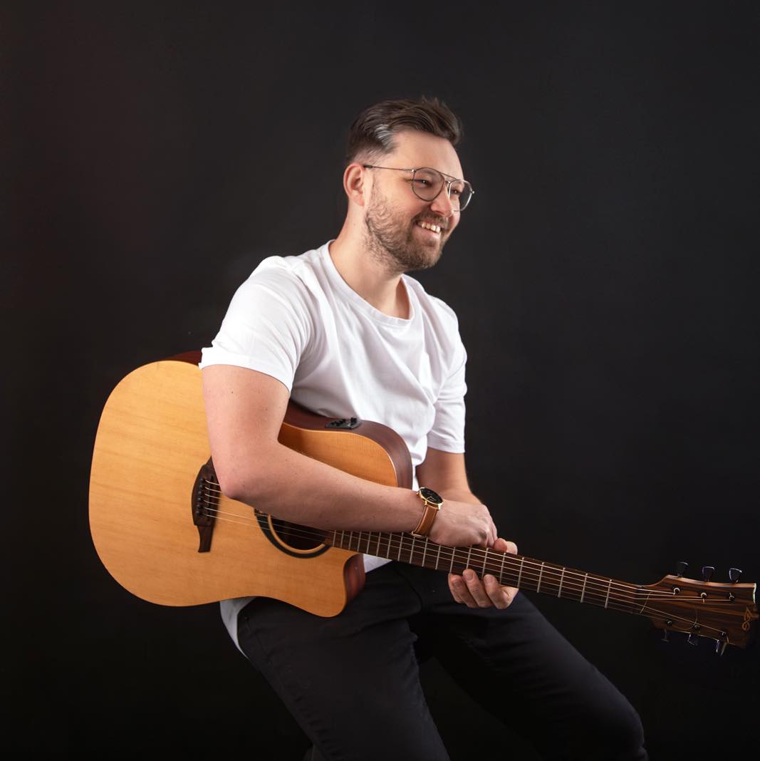 Tóth Árpád mosolyogva, akusztikus gitárral
